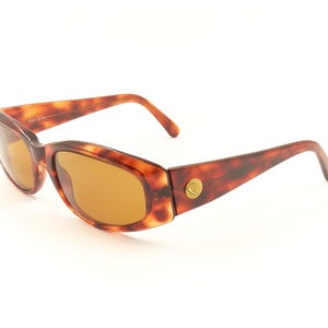 May include: Tortoise shell sunglasses with brown lenses. The sunglasses have a gold logo on the side.