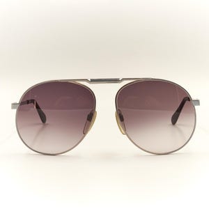 Pode incluir: Óculos de sol aviador prateados com lentes de degradê marrom.