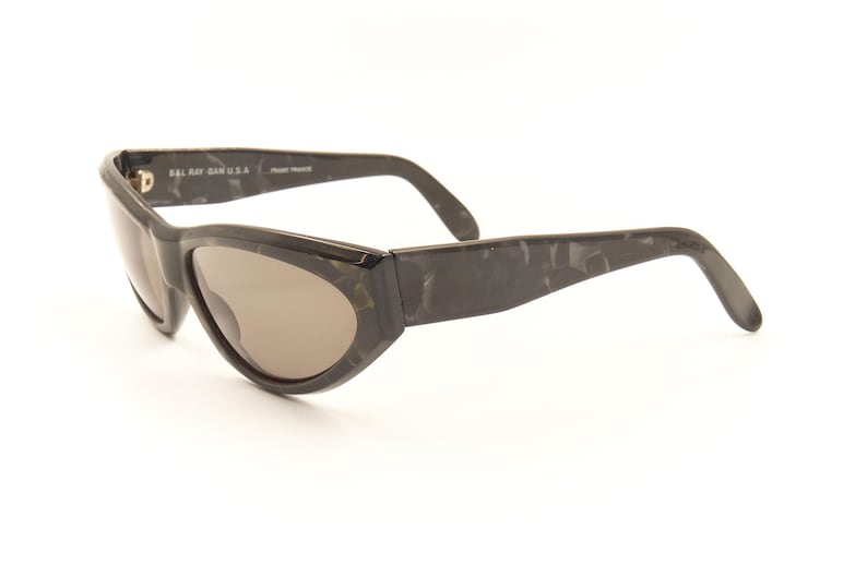 Pode incluir: &Oacute;culos de sol de tartaruga preta com arma&ccedil;&atilde;o curva e lentes marrons. Os &oacute;culos t&ecirc;m o texto "Bally Jan. U.S.A." na lateral.