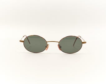 May include: A pair of oval-shaped sunglasses with a gold metal frame and dark green lenses.