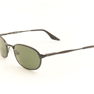 Pu&ograve; includere: Occhiali da sole ovali neri con lenti verdi. Le montature sono di colore metallico scuro e le aste sono sottili e dritte. Gli occhiali da sole hanno un design classico e sobrio, adatto all'uso quotidiano. Il testo "B&L RAY-BAN" &egrave; visibile sull'asta.