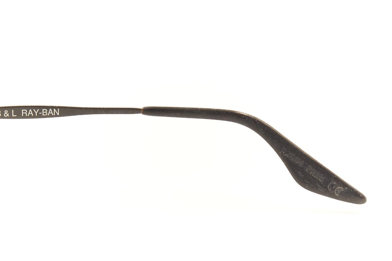 Pu&ograve; includere: Primo piano di un'asta di occhiali Ray-Ban grigio scuro. Il testo "B & L RAY-BAN" &egrave; stampato sull'asta. L'asta si curva verso il basso e termina con una punta arrotondata.