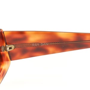 May include: A pair of brown tortoise shell Ray-Ban sunglasses with gold accents and brown lenses.