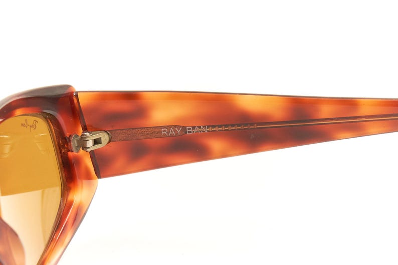 May include: A pair of brown tortoise shell Ray-Ban sunglasses with gold accents and brown lenses.