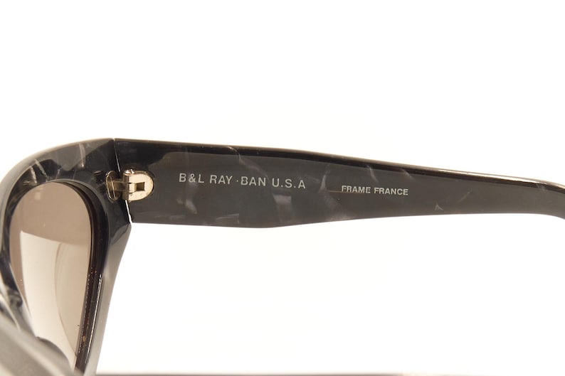 Pode incluir: &Oacute;culos de sol preto e cinza com padr&atilde;o de m&aacute;rmore com o texto "B&L RAY-BAN U.S.A. FRAME FRANCE" na lateral.