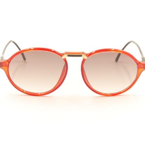 Puede incluir: Gafas de sol redondas rojas con un fino marco de metal y lentes tintados de color marrón.
