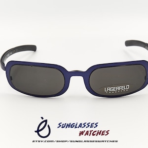 May include: Blue and black sunglasses with a rectangular frame and grey lenses. The sunglasses have the text "Lagerfeld" on the right lens.