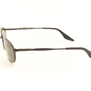 Pu&ograve; includere: Occhiali da sole con montatura in metallo nero e lenti ovali. Gli occhiali hanno un design elegante con aste sottili e un ponte. Le lenti sono di colore verde scuro e la montatura ha una finitura opaca. Il nome del marchio &egrave; visibile sull'asta.