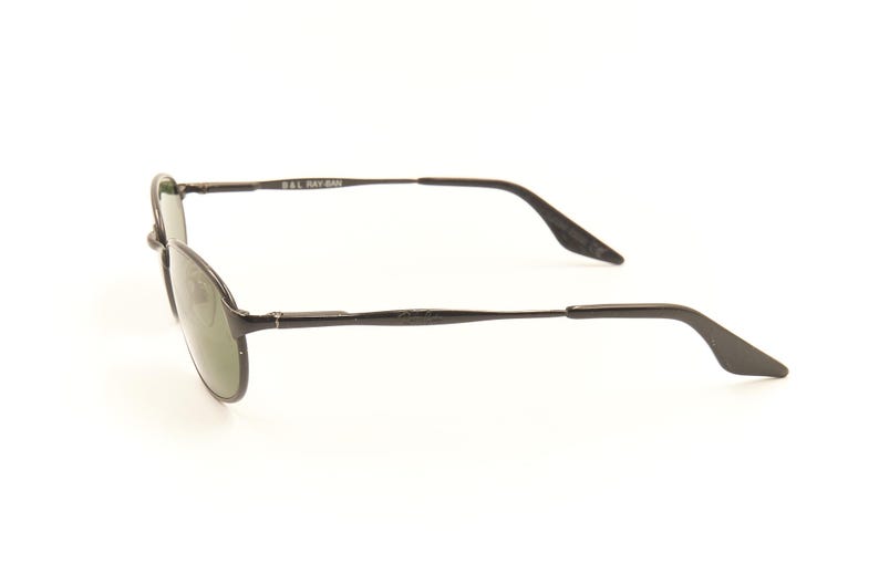 Pu&ograve; includere: Occhiali da sole con montatura in metallo nero e lenti ovali. Gli occhiali hanno un design elegante con aste sottili e un ponte. Le lenti sono di colore verde scuro e la montatura ha una finitura opaca. Il nome del marchio &egrave; visibile sull'asta.