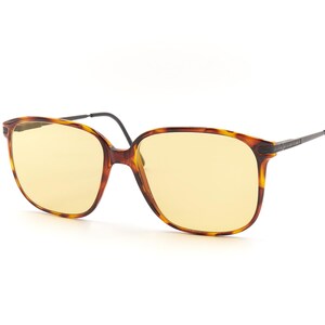 May include: A pair of tortoise shell eyeglasses with yellow lenses. The glasses have a square frame and black arms.