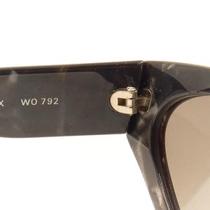 Pode incluir: &Oacute;culos de sol de tartaruga preto e cinza com dobradi&ccedil;a dourada. Os &oacute;culos t&ecirc;m lentes marrons e o texto "ONYX WO 792" est&aacute; impresso na arma&ccedil;&atilde;o.