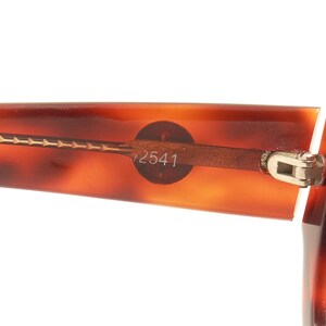 May include: Close-up of a tortoiseshell-patterned pair of eyeglasses with a gold metal frame and a hinge. The frame has the number "12541" printed on it.
