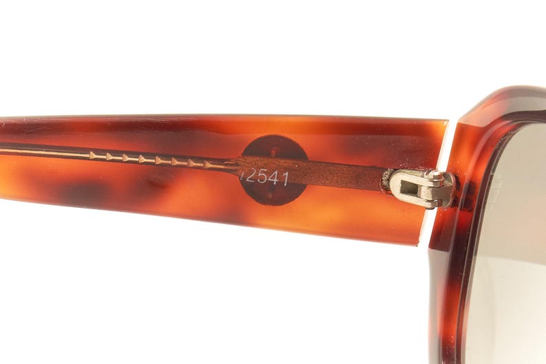 May include: Close-up of a tortoiseshell-patterned pair of eyeglasses with a gold metal frame and a hinge. The frame has the number "12541" printed on it.