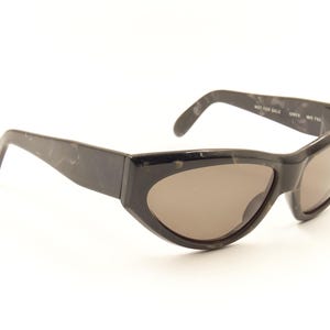 Pode incluir: &Oacute;culos de sol pretos de tartaruga com lentes marrons. Os &oacute;culos t&ecirc;m formato de olho de gato e uma arma&ccedil;&atilde;o fina.