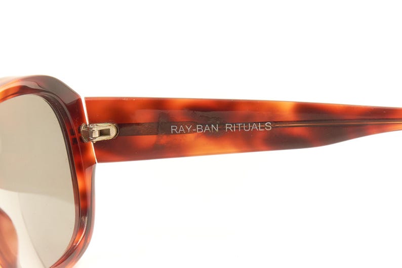 May include: Close-up of a pair of tortoiseshell sunglasses with the text "RAY-BAN RITUALS" on the frame.