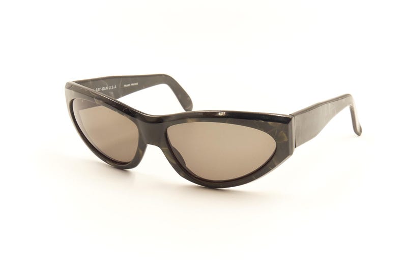 Pode incluir: &Oacute;culos de sol pretos de tartaruga com formato de olho de gato e lentes marrons.