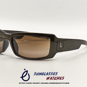May include: Brown rectangular sunglasses with brown lenses. The sunglasses have a black 'L' on the right side of the frame.