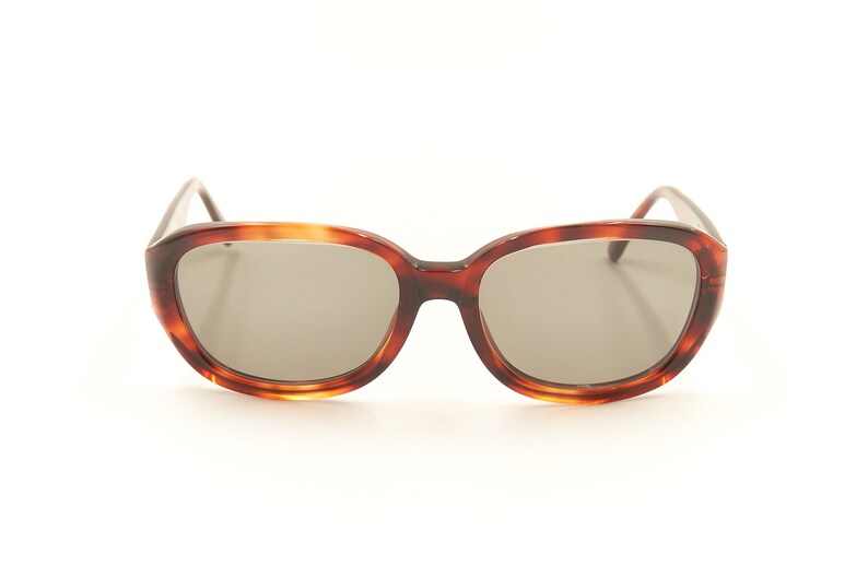 May include: Tortoise shell sunglasses with brown lenses. The sunglasses have a rounded, oval shape.