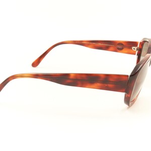 May include: Tortoise shell sunglasses with brown lenses. The sunglasses have a rectangular frame and are shown from the side.