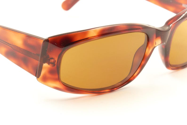 May include: Brown tortoise shell sunglasses with brown lenses. The sunglasses have a rectangular shape.