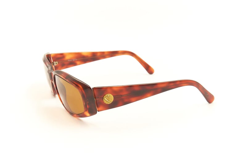 May include: Tortoise shell sunglasses with brown lenses. The sunglasses have a gold logo on the side.