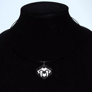 May include: A black choker necklace with a white pendant featuring a geometric design. The pendant is shaped like a heart with a stylized letter M inside.