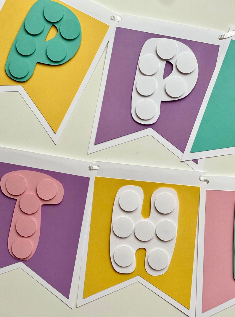 Pode incluir: Uma faixa colorida com a palavra "Happy" escrita em letras brancas com c&iacute;rculos brancos em um fundo roxo, amarelo e verde.