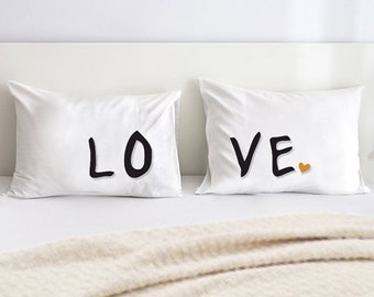 May include: Two white pillowcases with the word "LOVE" printed in black. The word is split between the two pillowcases, with "LO" on one pillowcase and "VE" on the other. A small orange heart is printed next to the "VE".