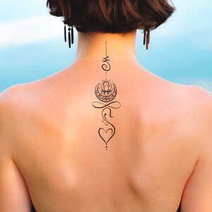 Pu&ograve; includere: Una donna con un tatuaggio nero sulla schiena. Il tatuaggio &egrave; un disegno verticale con un fiore di loto, una luna crescente, un simbolo di infinito e un cuore.