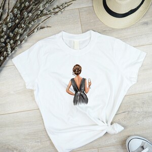 May include: White t-shirt with a graphic of a woman in a black dress holding a glass of champagne.