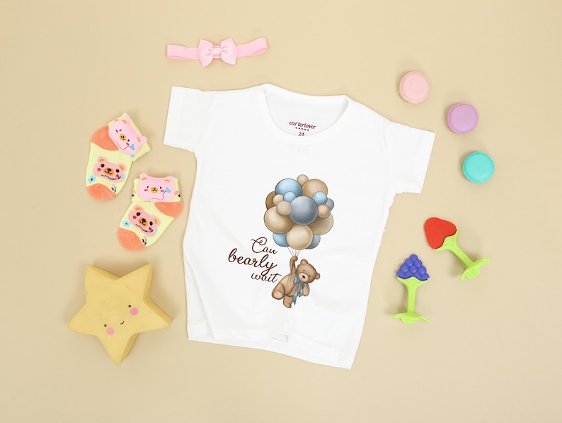 May include: White baby onesie with a brown bear holding balloons that say "Can bearly wait". The onesie is surrounded by a pink headband, yellow star, and colorful macarons.