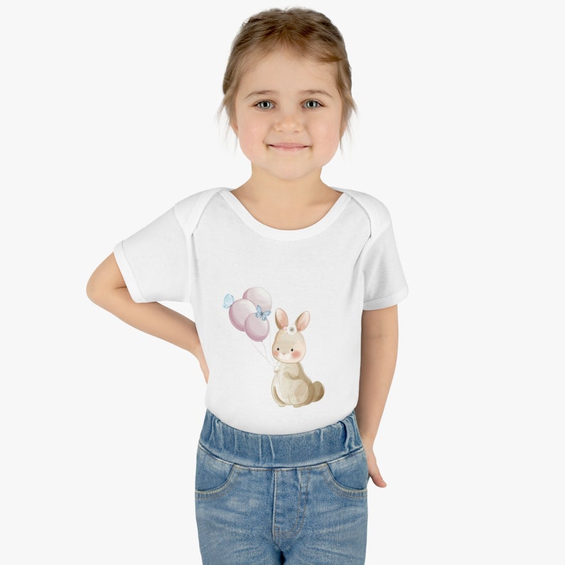 May include: A white baby onesie with a brown bunny holding pink balloons. The bunny has a blue bow on its head.