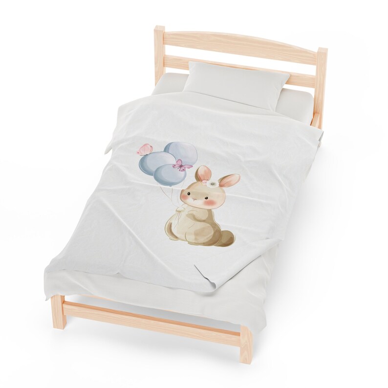 May include: A white and blue bunny with a pink flower on its head holds blue balloons with pink butterflies. The bunny is on a white blanket on a wooden bed frame.
