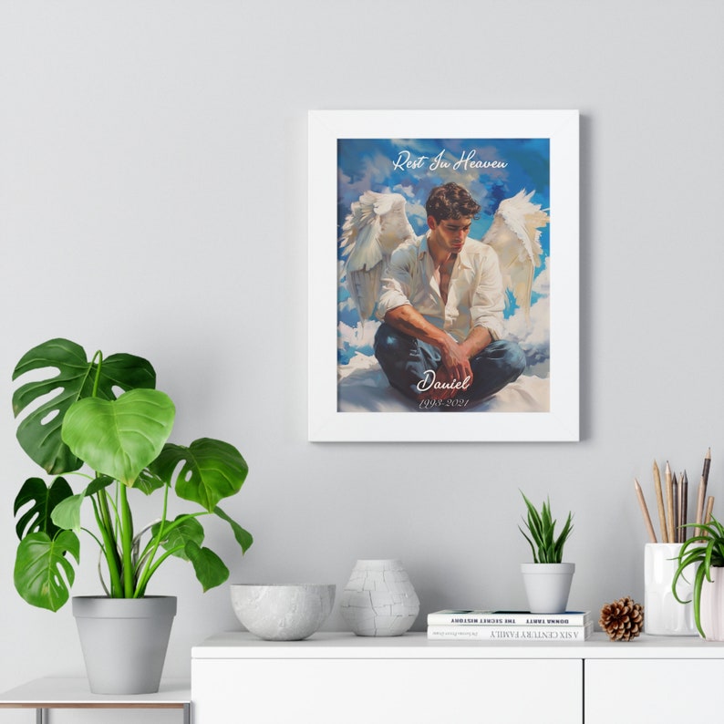 May include: A framed print of a man with angel wings sitting on clouds. The print has the text "Rest In Heaven" and "Daniel 1993-2021".