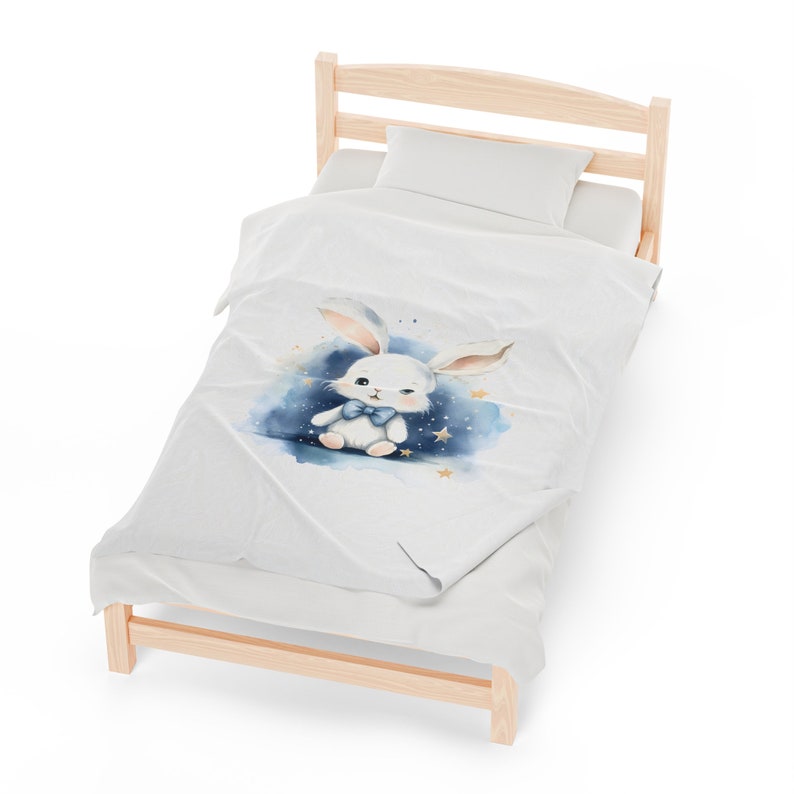 Pu&ograve; includere: Un letto bianco con una federa a motivi bianchi e blu con un coniglio dei cartoni animati con un papillon blu. La federa ha un effetto acquerello con stelle dorate.