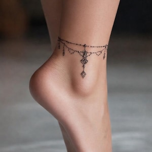 Può includere: Delicato tatuaggio nero alla caviglia con un design simmetrico. Presenta forme a diamante e elementi a goccia pendenti. Il tatuaggio è sulla caviglia.