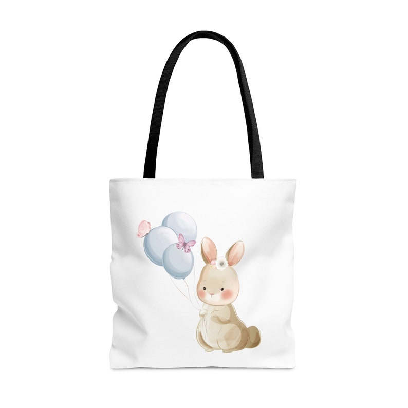 May include: A white tote bag with black handles features a watercolor illustration of a brown bunny holding blue balloons with pink butterflies. The bunny is wearing a white flower crown.