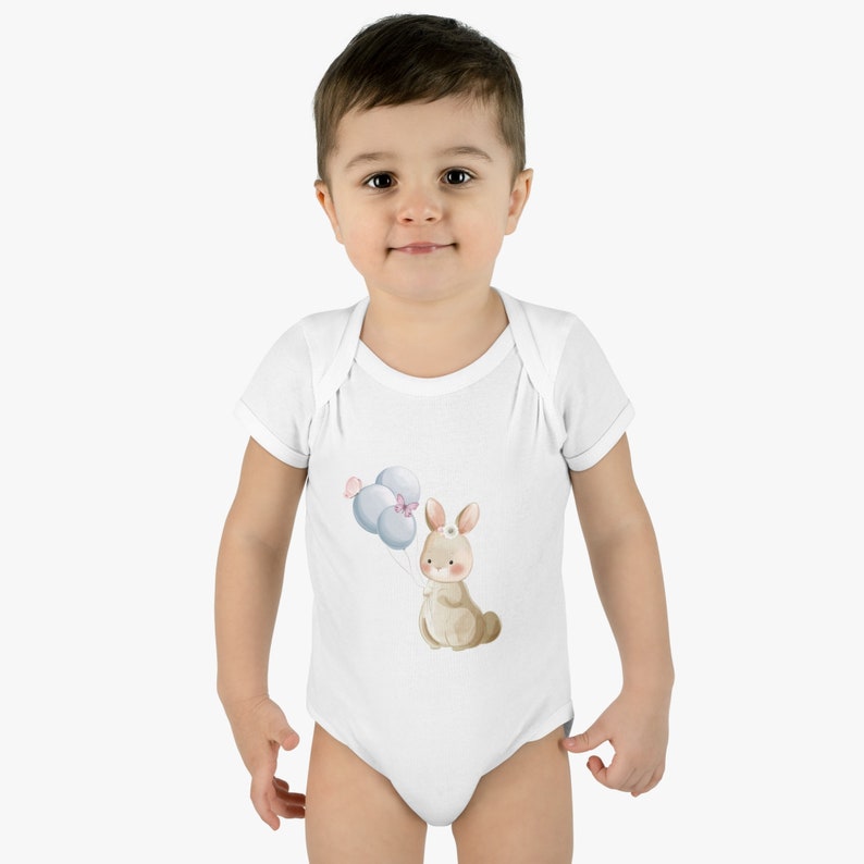 May include: A white baby onesie with a brown bunny holding blue balloons. The bunny has a pink bow on its head.
