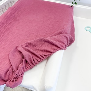 Op de afbeelding: Een roze hoeslaken voor een verschoningsmat. Het laken is gemaakt van een zachte, gestructureerde stof.