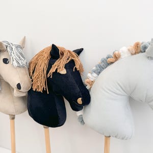 Puede incluir: Tres caballos de peluche en palos de madera. Los caballos son grises, negros y marrones con crines y colas de diferentes colores.