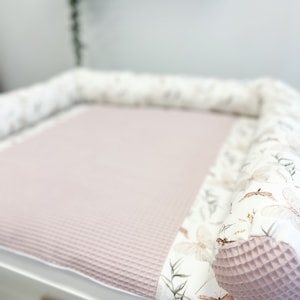 Op de afbeelding: Een roze en witte verschoningmat met een wafelstructuur en een bloemenprint met vlinders en bladeren. De verschoningmat is omgeven door een witte, gevoerde rand.