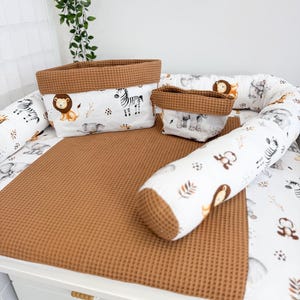 May include: A baby changing station with a brown waffle-textured changing mat and matching storage baskets. The baskets and bumpers feature a white fabric with safari animal illustrations. A brown bolster pillow completes the set.