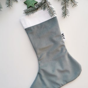 Op de afbeelding: Een grijze kerstsok met een witte boord. De sok heeft een textuur en het woord "Kels" staat op de zijkant.