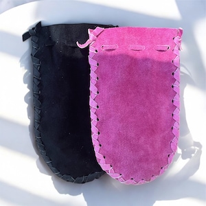 May include: Two suede pouches with braided trim. One pouch is black and the other is pink.