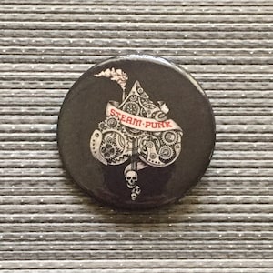 May include: A black button with a white and gray steampunk design of a spade with gears and a skull. The text "STEAM-PUNK" is written on a banner.
