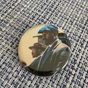 May include: A round button featuring a sepia-toned image of two men in suits and hats. The man in the foreground wears a blue cap and a gray suit. The second man wears a brown hat and a dark suit. The button has a glossy finish.