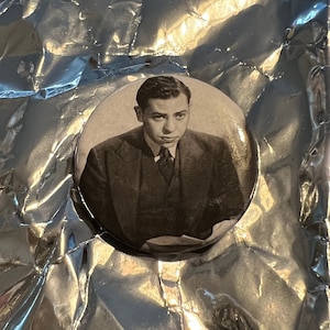 May include: A black and white photo of a man wearing a suit and tie. The photo is on a round button.