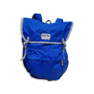 May include: A blue rucksack with a grey trim and a Kohl's Bergsport logo. The rucksack has a zipped pocket on the front.