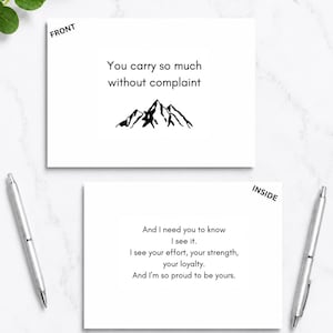 May include: A white greeting card with black text and a mountain graphic. The front reads: You carry so much without complaint. The inside reads: And I need you to know I see it. I see your effort, your strength, your loyalty. And I'm so proud to be yours.