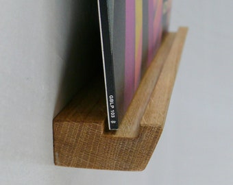 May include: A wooden record shelf with a vinyl record leaning against it. The record has a colorful abstract design and the text "GBLP 103" printed on the spine.